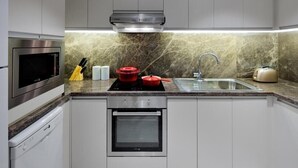 A modern kitchen with a built-in oven, microwave, and dishwasher, a granite countertop, and a stainless steel sink. - 1 Bedroom Apartment Near Gold Souk Metro BY E R (Dubai)