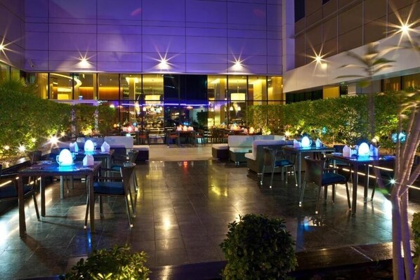 Un área de comedor al aire libre con mesas y sillas, rodeada de follaje e iluminada con luces en forma de estrella.
