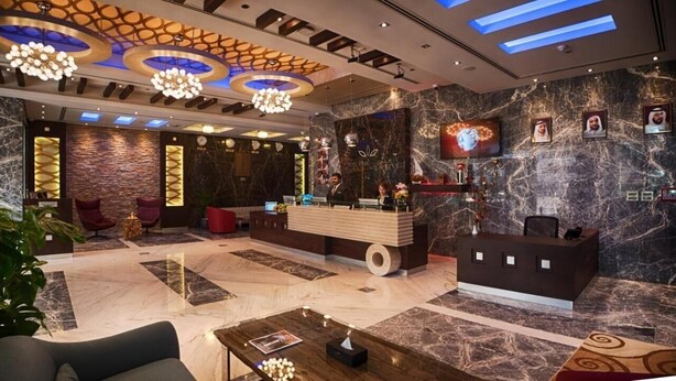 A modern hotel lobby with marble flooring, a reception desk, seating areas, and a large TV screen. - Deluxe Room Near Mashreq Metro Station By E R (Dubai)