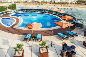 Un espace piscine doté de chaises longues et de parasols, entouré d’une terrasse carrelée et agrémenté de plantes en pot.