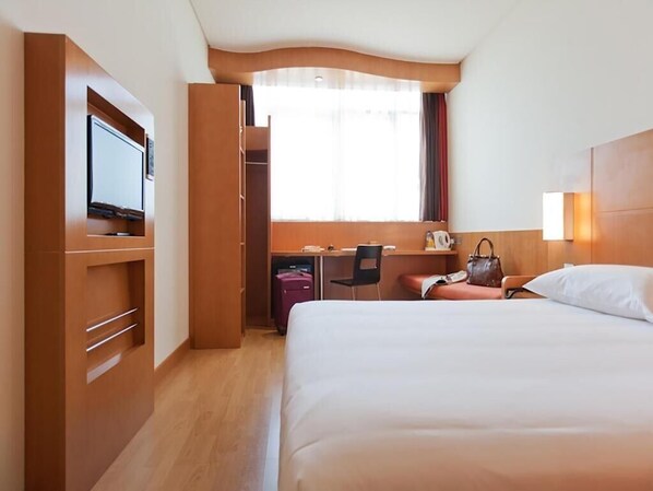 Une chambre d’hôtel comprenant un lit, un bureau, une chaise, une télévision et une armoire.