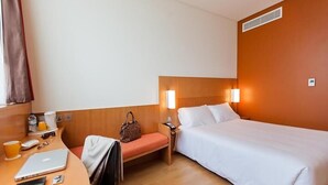 A hotel room with a bed, a desk with a laptop, a chair, a bedside table with a lamp, and a window with curtains. - Standard Room Near Rabdan Majlis By E R (Area)
