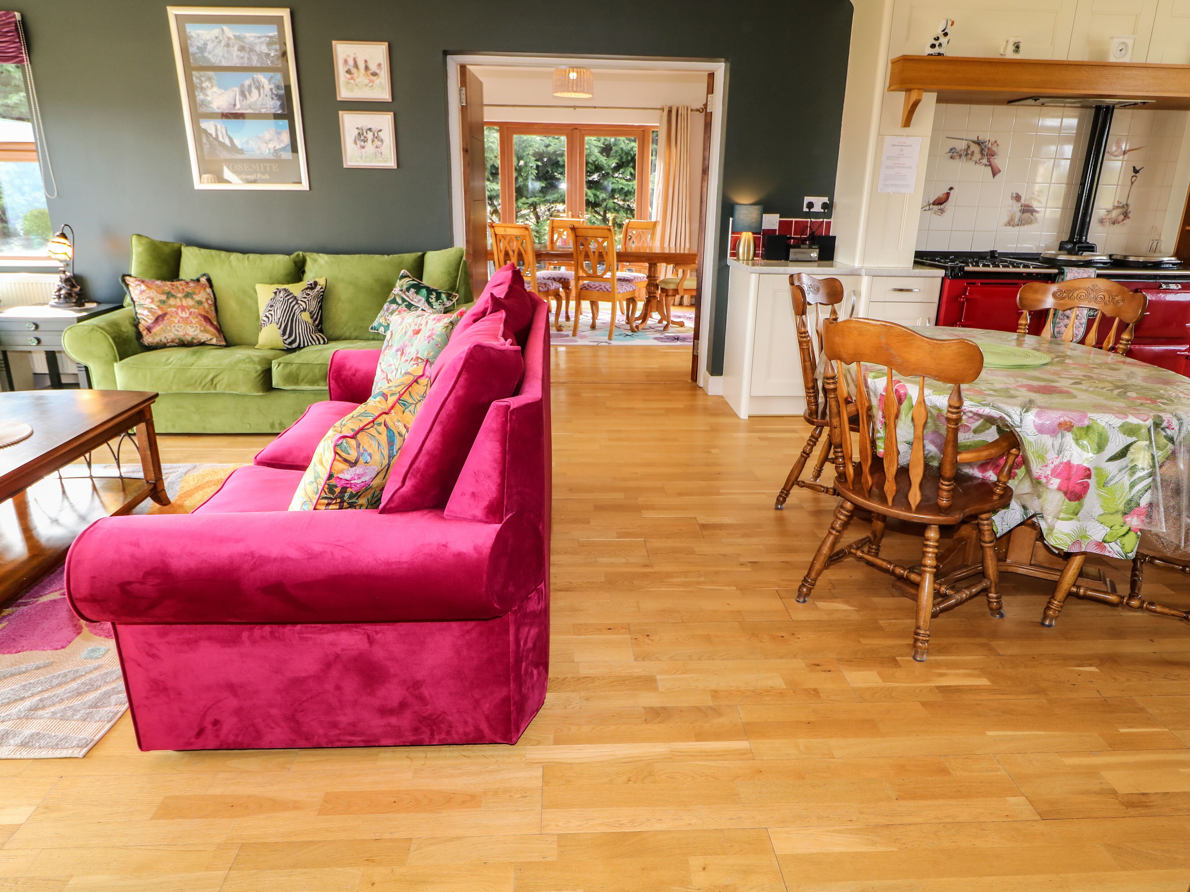 A living room with a green sofa and a pink sofa, wooden dining table, and chairs.
