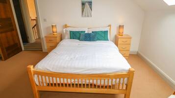 Un dormitorio con una cama de madera, dos mesitas de noche con lámparas, vistas a una terraza de madera y una escalera que conduce a otra habitación.