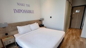 A hotel room with a large bed, a nightstand, a wall-mounted lamp, and a door with a sign.