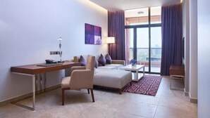 A modern hotel room with a desk, sofa, and a large window offering a city view. - Two Bedroom Suite Near Dic Metro (Dubai)
