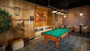 A pool table in a room with wooden walls, a brick wall, and a sofa with cushions. - Studio Apartment in Mirdif By E R (Dubai)