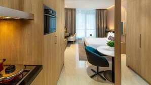 A modern hotel room with a kitchen area, a dining table with chairs, a bed, and a large window with curtains. - Studio Apartment in Mirdif By E R (Dubai)