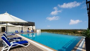 A swimming pool with lounge chairs, a covered area, and a view of the landscape. - Studio Apartment in Mirdif By E R (Dubai)