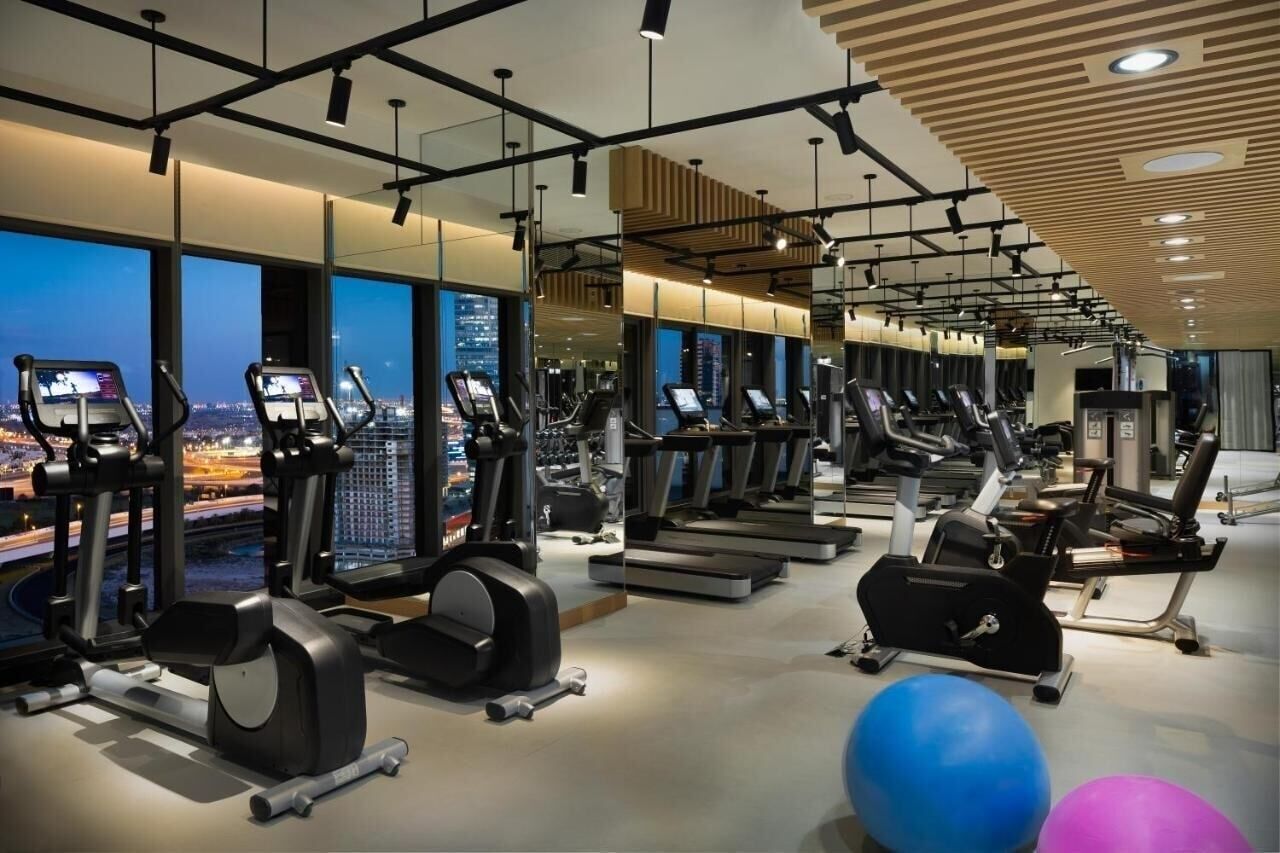 Et moderne fitnesscenter med løbebånd, crosstrainere og vægte, med store vinduer og udsigt over byen.