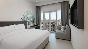 Une chambre d’hôtel moderne dotée d’un grand lit, d’un coin salon avec vue sur la ville et d’un téléviseur à écran plat fixé au mur.