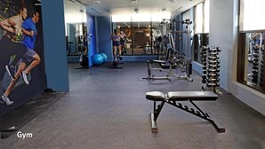 Een sportschool met fitnessapparatuur, een bank en een spiegelwand.