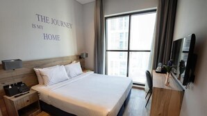 Een hotelkamer met een groot bed, een nachtkastje met een telefoon en een lamp, een aan de muur bevestigde televisie en een raam met gordijnen.