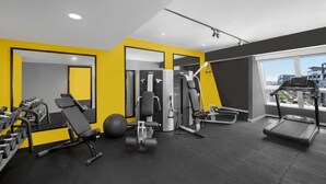 A modern gym with various exercise equipment, a treadmill, and a large window offering a city view. - Deluxe Room Near Burj Khalifa Metro By E R (Dubai)