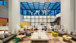 A spacious lobby with a high ceiling, a central seating area with sofas and chairs, a staircase, and a reception desk. - Two Bedroom Apartment Near Moe By E R (Dubai)