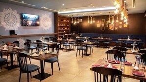 Een restaurant met meerdere eettafels en stoelen, een aan de muur bevestigde televisie en decoratieve muurkunst.
