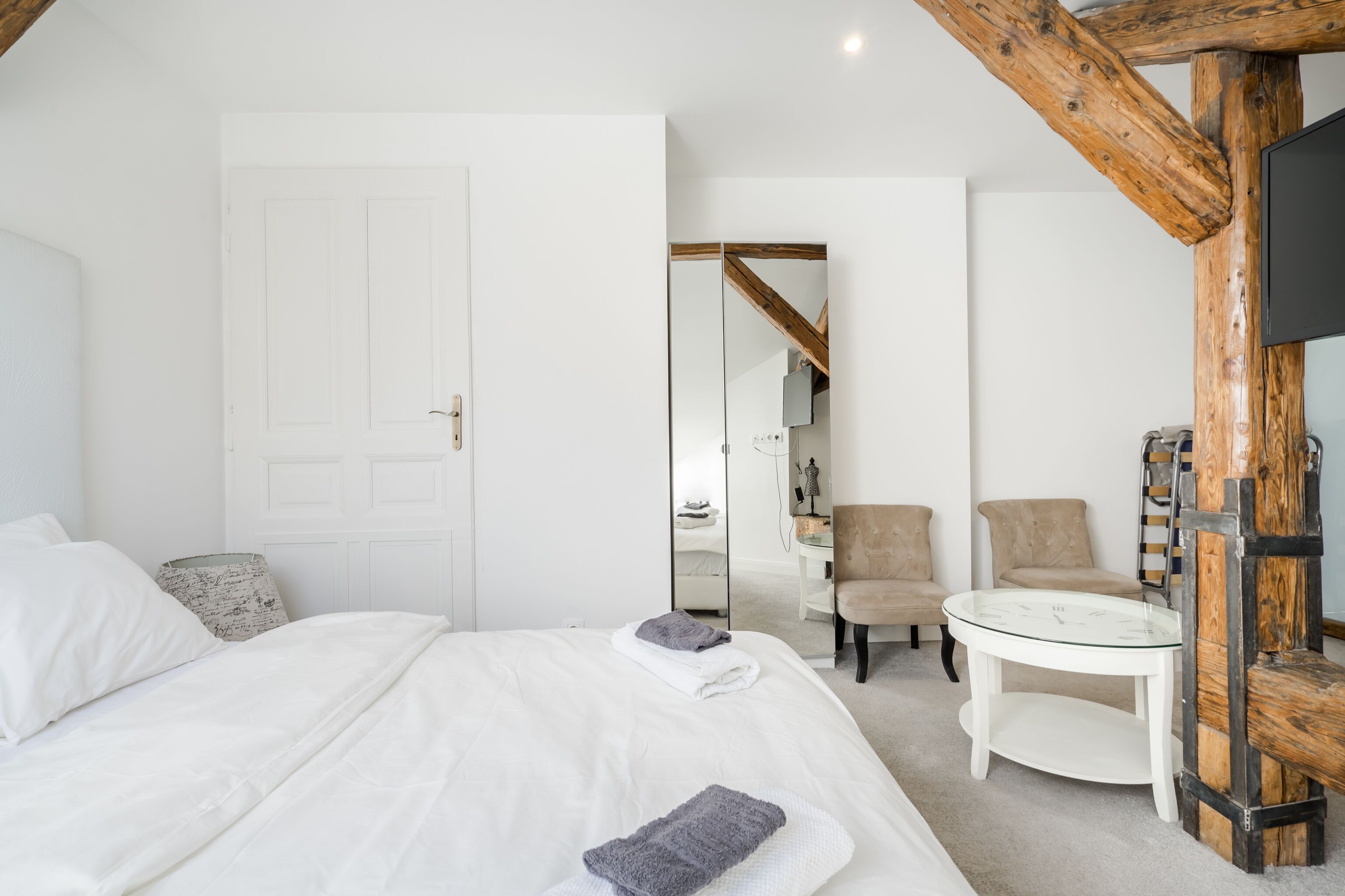 Un dormitorio con una cama grande, una mesita redonda pequeña, una silla y estructura de vigas de madera.