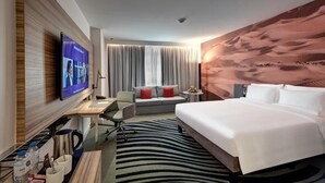 A modern hotel room with a large bed, a desk with a flat-screen TV, a sofa, and a large window with curtains. - Standard Room Near Sharjah Expo Centre By E R (Sharjah)