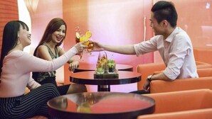 Un grupo de personas brindando con bebidas alrededor de una mesa en un moderno salón con asientos naranjas.