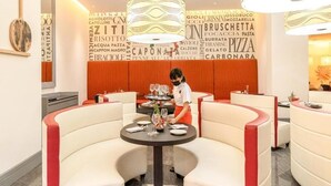 Un restaurante con una decoración moderna, que presenta asientos curvos blancos y rojos, una mesa redonda central con vasos y platos, y una pared con palabras relacionadas con la comida.