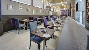 Une grande salle à manger avec des rangées de tables et de chaises, un mur orné de motifs et un plafond doté d’un éclairage encastré.