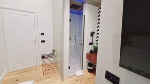 A hotel room with a wooden floor, a bed, a TV, a shower area, and a small table with a plant. - B&B SirenaResina - Ligea Standard room (Ercolano)