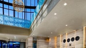 A modern hotel reception area with a marble counter, a glass wall, and a high ceiling with natural light.
