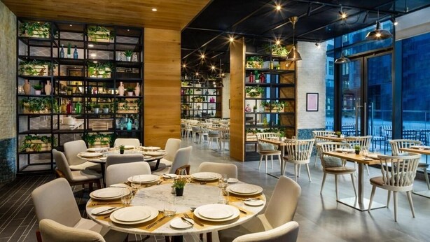 A restaurant with round tables set for dining, surrounded by shelves of plants and books.