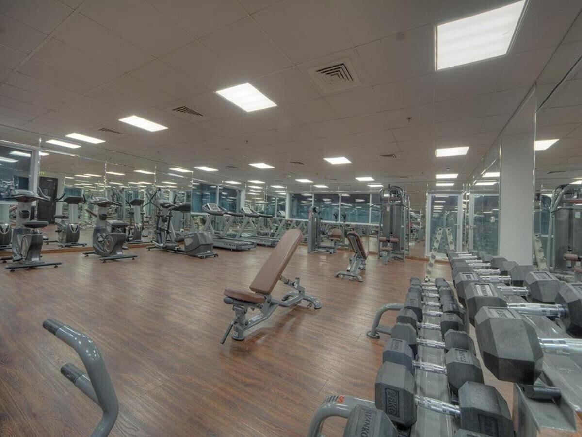 Et stort fitnessrum med forskellig træningsudstyr, herunder løbebånd, motionscykler og vægte.