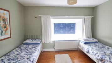 Una habitación con dos camas individuales, un radiador, una ventana con cortinas, una lámpara colgante y un cuadro en la pared.