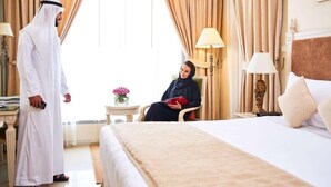 Une chambre d’hôtel comprenant un lit, un coin salon avec un fauteuil, une lampe et des rideaux.
