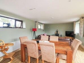 Un salon chaleureux avec une table à manger en bois, des chaises beiges, un lampadaire rouge, un canapé, un téléviseur et un poêle à bois.