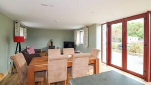 Un área de comedor con una mesa y sillas de madera, un televisor y vistas al exterior a través de grandes puertas correderas de vidrio.