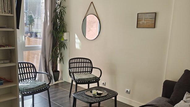 Una sala de estar con un sofá, dos sillones, una mesita de centro, una estantería, un espejo y una planta en maceta.