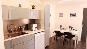 Una cocina compacta con lavavajillas, microondas y un lavabo. Hay una zona de comedor con una mesa y sillas.