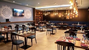 Ein Restaurant mit mehreren Tischen, Stühlen, einem an der Wand befestigten Fernseher und dekorativen Wandmustern.