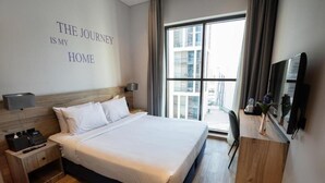 Ein Hotelzimmer mit einem großen Bett, einem Nachttisch mit Telefon, einem Fernseher auf einer Holzkommode und einem Fenster mit Blick auf die Stadt.