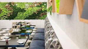 A modern indoor dining area with a checkered floor, black and grey upholstered seating, and a green wall with plants. - Standard Room Near Port Saeed Plaza By E R (Dubai)