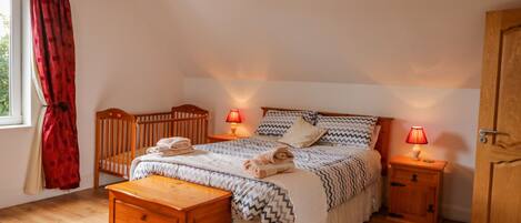 A bedroom with a wooden bed, two bedside tables with lamps, a wooden dresser, and a window with red curtains.