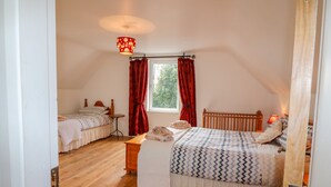 Une chambre avec deux lits, une fenêtre avec des rideaux rouges, une petite table et un luminaire au plafond.