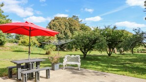 Une terrasse extérieure avec une table de pique-nique, un banc et un parasol rouge.