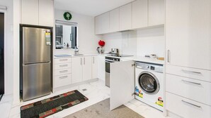 A modern kitchen with white cabinets, a stainless steel refrigerator, a built-in oven, and a washing machine. - Stunning 2BR in Kelston with WIFI and Carpark (Auckland West)
