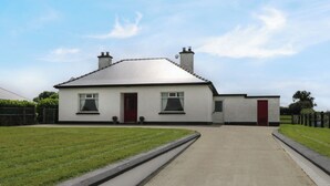A two-story house with a red door, a small attached garage, and a paved driveway leading to the front door. - KATE'S COTTAGE, pet friendly, with open fire in Ballina, County Mayo (Ballina)