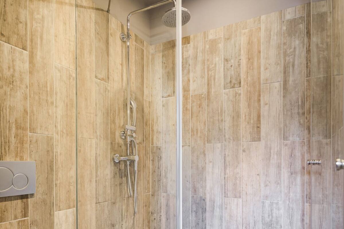 A modern bathroom with a glass-enclosed shower, a toilet, and wooden wall tiles.