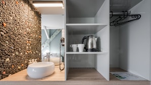 A modern bathroom with a stone wall, a white sink, and a shelf with a kettle and cups. - Butik Apartments by BQA (Budapest)