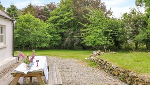A wooden picnic table with a white tablecloth, a potted plant, and a wine glass. - THE OLD WHITE COTTAGE, pet friendly in Shillelagh, County Wicklow (Shillelagh)