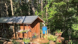 A wooden cabin with a metal roof, surrounded by a garden with various potted plants and flowers. - Beautiful & peaceful cabin w deck, garden, firepit & walking trails. (Murphy)