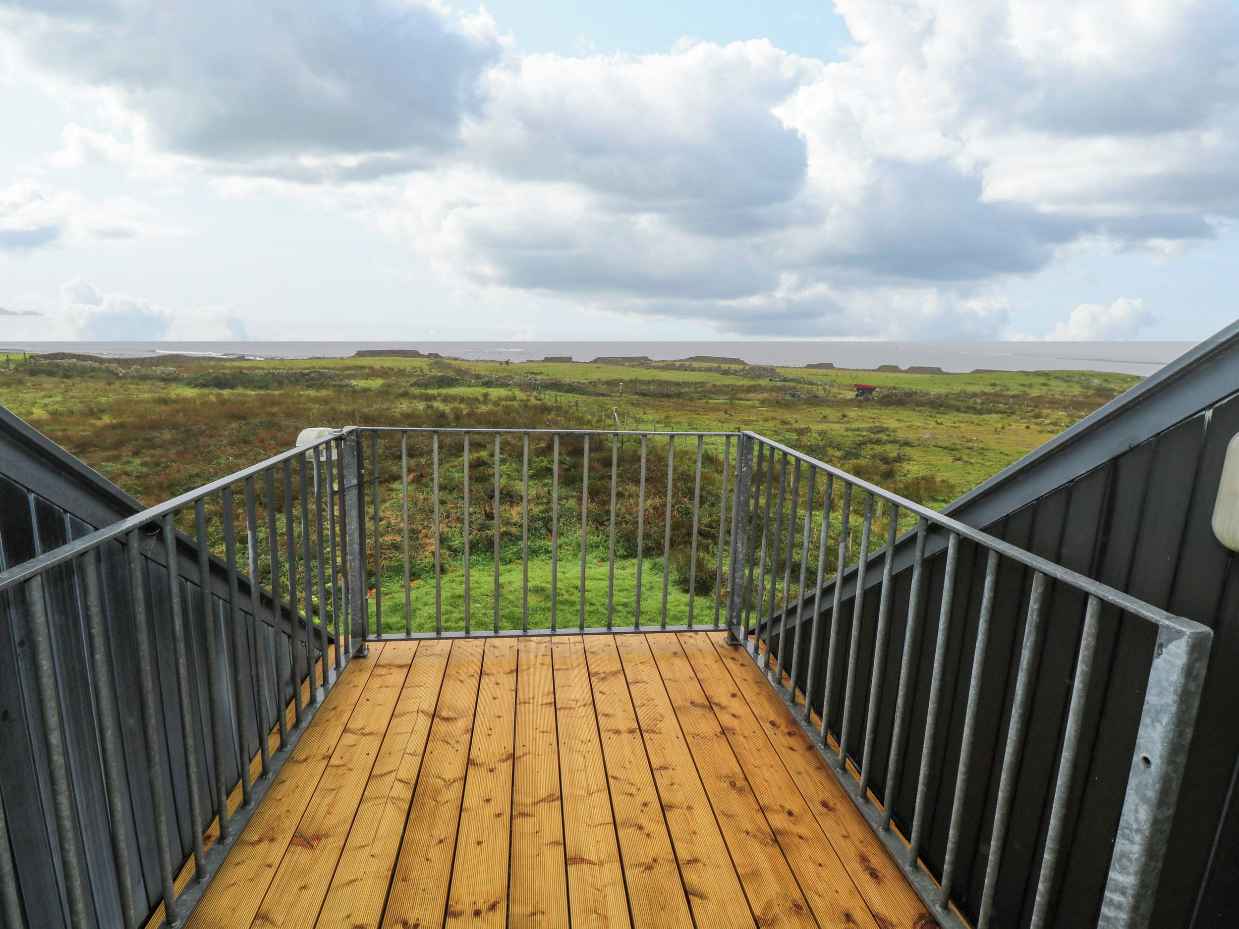 A wooden deck with metal railings leading to a grassy landscape with distant hills.