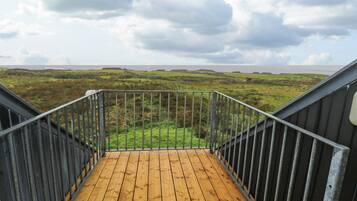 A wooden deck with metal railings leading to a grassy landscape with distant hills.