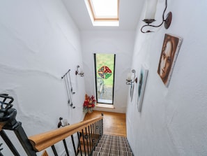 A narrow stairway with a wooden handrail, a small window with a stained glass design, and wall-mounted decor including a candle holder and a framed picture. - OCEAN SAIL HOUSE, pet friendly in Dungloe, County Donegal (Dungloe)